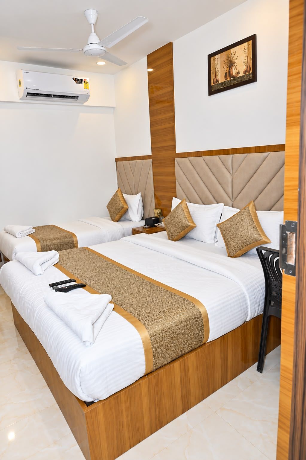 Une chambre d’hôtel avec deux lits, un ventilateur de plafond, un appareil de climatisation et une œuvre d’art encadrée au mur.