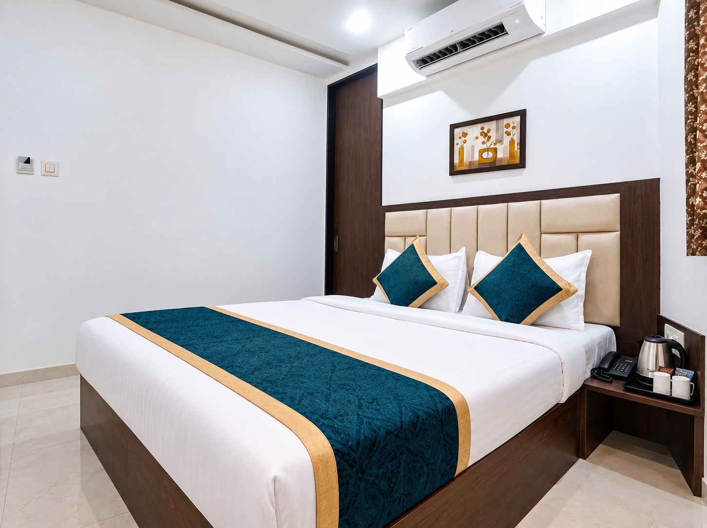 Una habitación de hotel con una cama, una mesita de noche, un equipo de aire acondicionado, una obra de arte en la pared y una puerta.