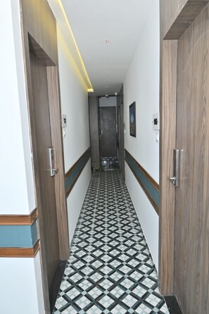 A hallway with a patterned floor, wooden doors, and a ceiling with recessed lighting. - HOTEL SHAHI PALACE (Mumbai)