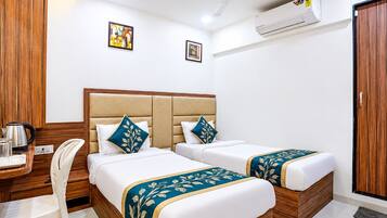 A hotel room with two beds, a desk with a kettle, a chair, and an air conditioning unit.