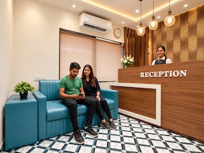 A reception area with a blue sofa, a reception desk labeled 'RECEPTION,' and an air conditioning unit on the wall.
