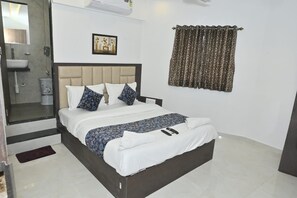 A hotel room with a bed, bedside table, and a bathroom with a sink and toilet. - HOTEL SHAHI PALACE (Mumbai)