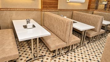 Un interior de restaurante con asientos tipo cabina, mesas blancas, baldosas de piso estampadas y unidades de aire acondicionado fijadas a la pared.