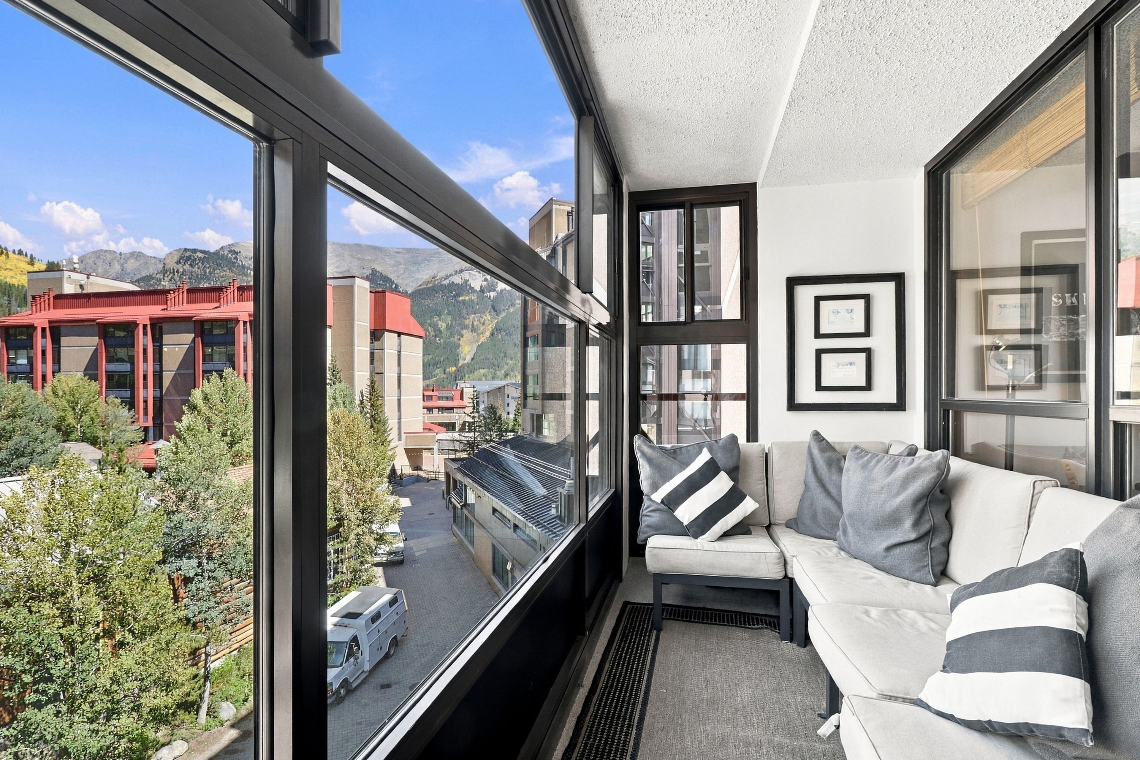 A modern interior with a balcony, a sofa, and a view of a cityscape and mountains.