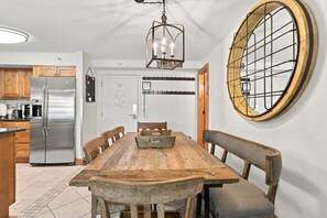 A kitchen with a stainless steel refrigerator, wooden cabinets, a dining table with chairs, and a large round mirror on the wall. - Mountain Plaza Escape, Hot Tub, Parking, Mountain and Lake Views (Copper Mountain)