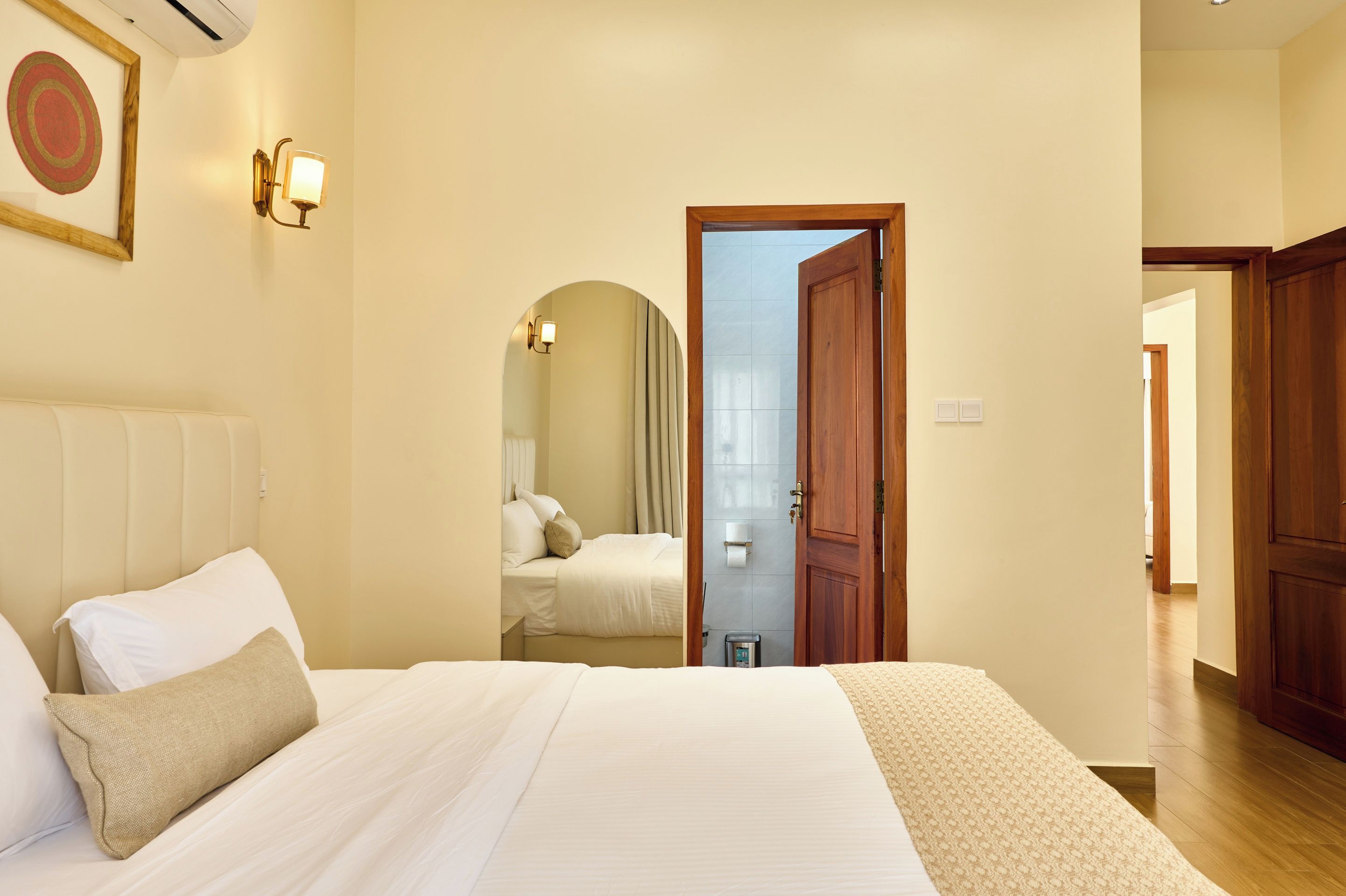 Una habitación de hotel con una cama, una puerta de madera y un baño visible a través de un arco.