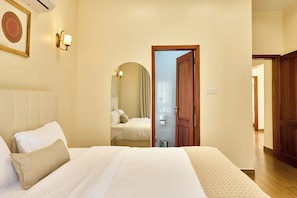 Habitació d'hotel amb un llit, una porta de fusta i un bany visible a través d'una volta.