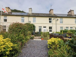A residential building with a gravel pathway, a wooden fence, and various plants. - 8 Railway Cottages (Ulverston)