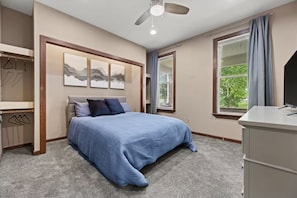 Ein Schlafzimmer mit einem Bett, einem Deckenventilator, einem Schreibtisch und einem Fenster mit Vorhängen.