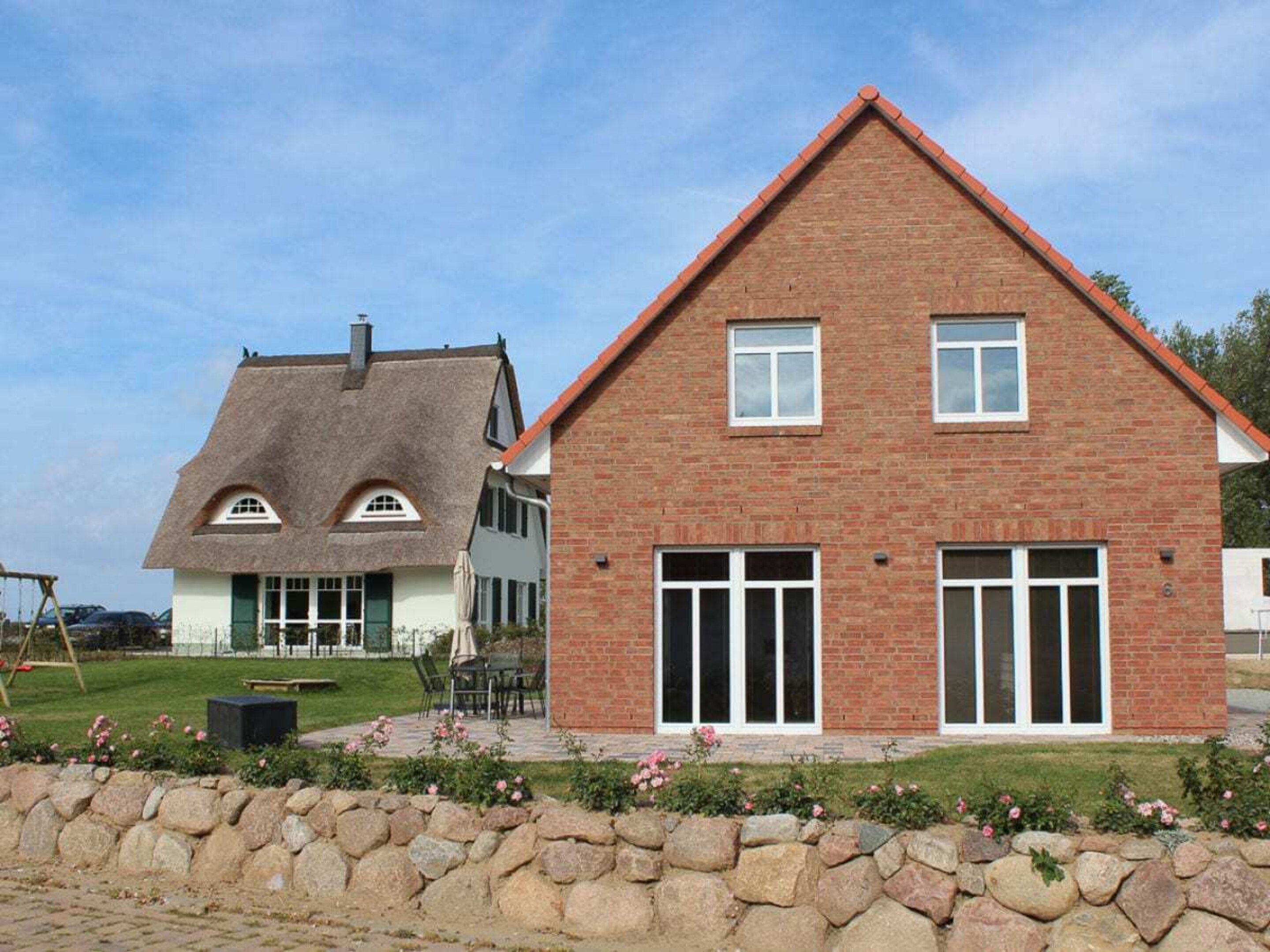 A two-story house with a brick facade, large windows, and a stone wall in front.
