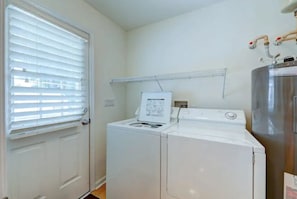 A laundry room with a front-loading washer and dryer, a metal shelving unit, and a water heater. - Coastal Charm Near the Beach in Rehoboth (Rehoboth Beach)
