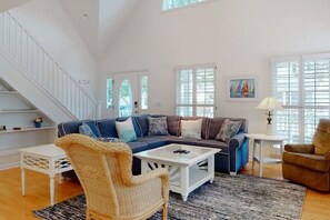 A spacious living room with a blue sofa, white coffee table, wicker chair, and a staircase. - Coastal Charm Near the Beach in Rehoboth (Rehoboth Beach)