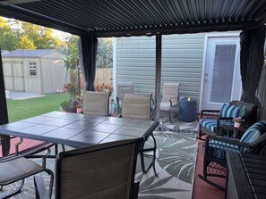 Een terras buiten met een tafel en stoelen, een overdekte zithoek, en uitzicht op de achtertuin.
