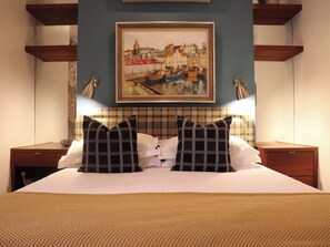 A hotel room with a bed, two nightstands, a painting on the wall, and a plaid headboard. - De Waterkant Guest Suites - WS03 (Cape Town)