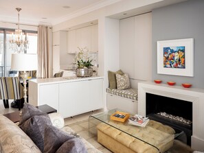 A modern living room with a glass coffee table, a sofa, a fireplace, and a kitchen area with a dining table and chairs. - De Waterkant Guest Suites - WS03 (Cape Town)