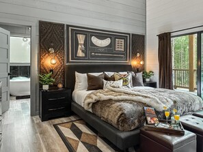 Ein modernes Schlafzimmer mit einem großen Bett, Nachttischen, einem Beistelltisch, einem gerahmten Bild über dem Bett und einem Fenster mit Vorhängen.