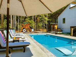 Ein Schwimmbecken mit Liegestühlen und einer Spielanlage für Kinder.