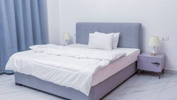 Un letto con una testiera grigia, biancheria da letto bianca e due comodini con lampade.