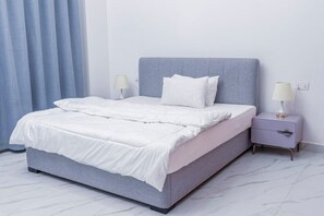 Un letto con una testiera grigia, biancheria da letto bianca e due comodini con lampade.