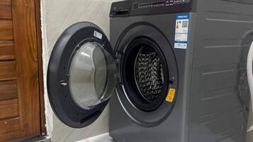 Eine Waschmaschine mit Frontöffnung in einem Badezimmer, mit Holztür und gefliesten Wänden.