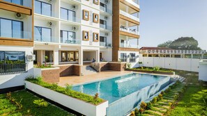 Un hotel moderno con piscina, diversi balconi e un giardino curato.