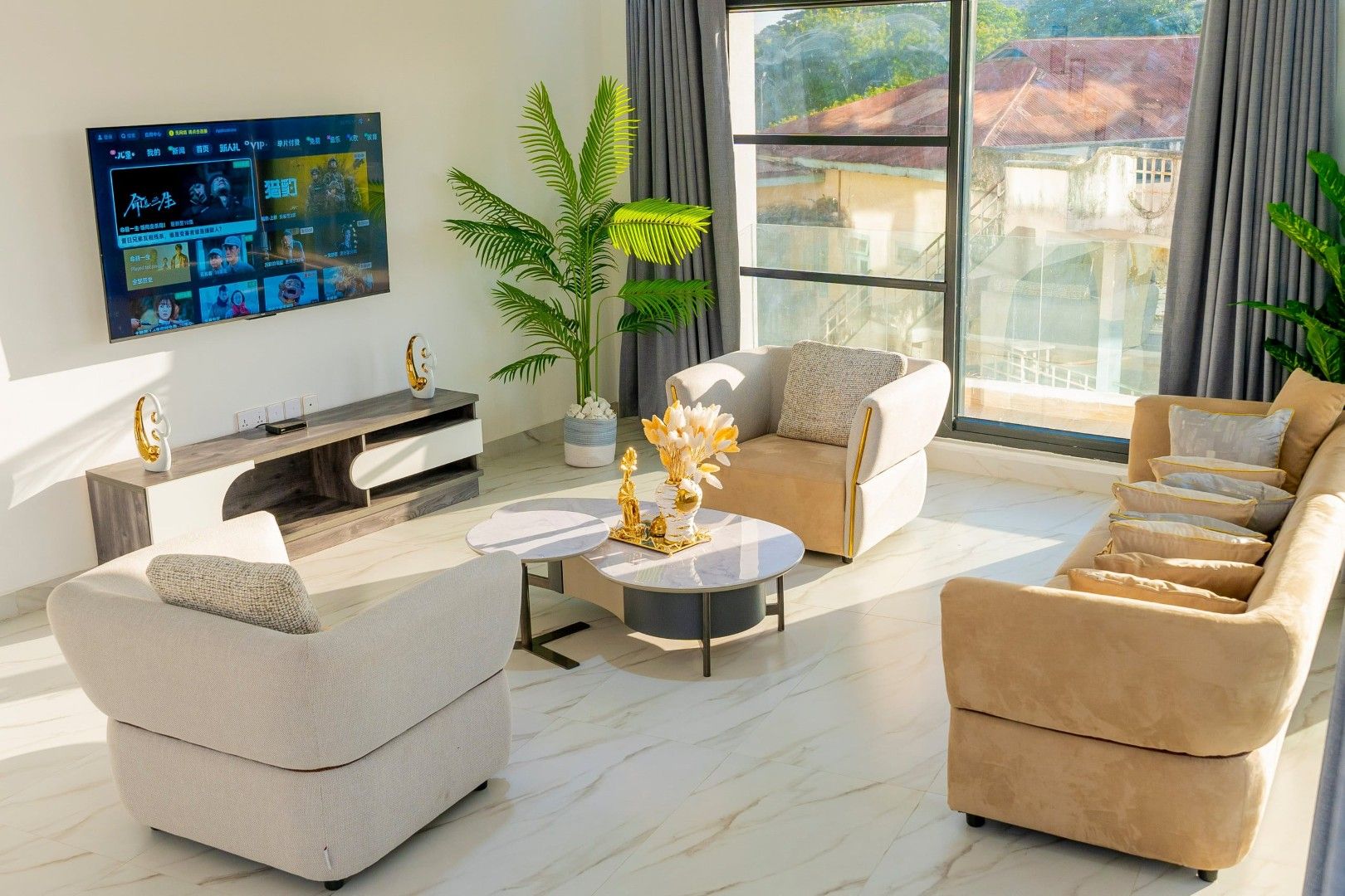 Un soggiorno moderno con una TV a schermo piatto fissata al muro, un divano, un tavolino da caffè e una grande finestra con vista sugli edifici.