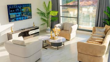 Un soggiorno moderno con una TV a schermo piatto fissata al muro, un divano, un tavolino da caffè e una grande finestra con vista sugli edifici.