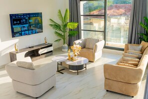 Un soggiorno moderno con una TV a schermo piatto fissata al muro, un divano, un tavolino da caffè e una grande finestra con vista sugli edifici.