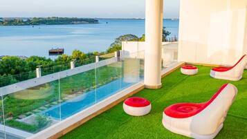 Ein Pool auf dem Dach mit Glasumrandung, grünem Kunstrasen und roten und weißen Liegestühlen.