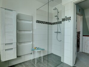 Ein modernes Badezimmer mit Duschkabine aus Glas, einem weißen Heizkörper und einem kleinen Hocker.