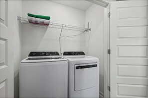 A laundry room with two front-loading washing machines and a drying rack with folded clothes. - The Cove-3-bedroom townhome in Orange Beach. Pet friendly! (Orange Beach)