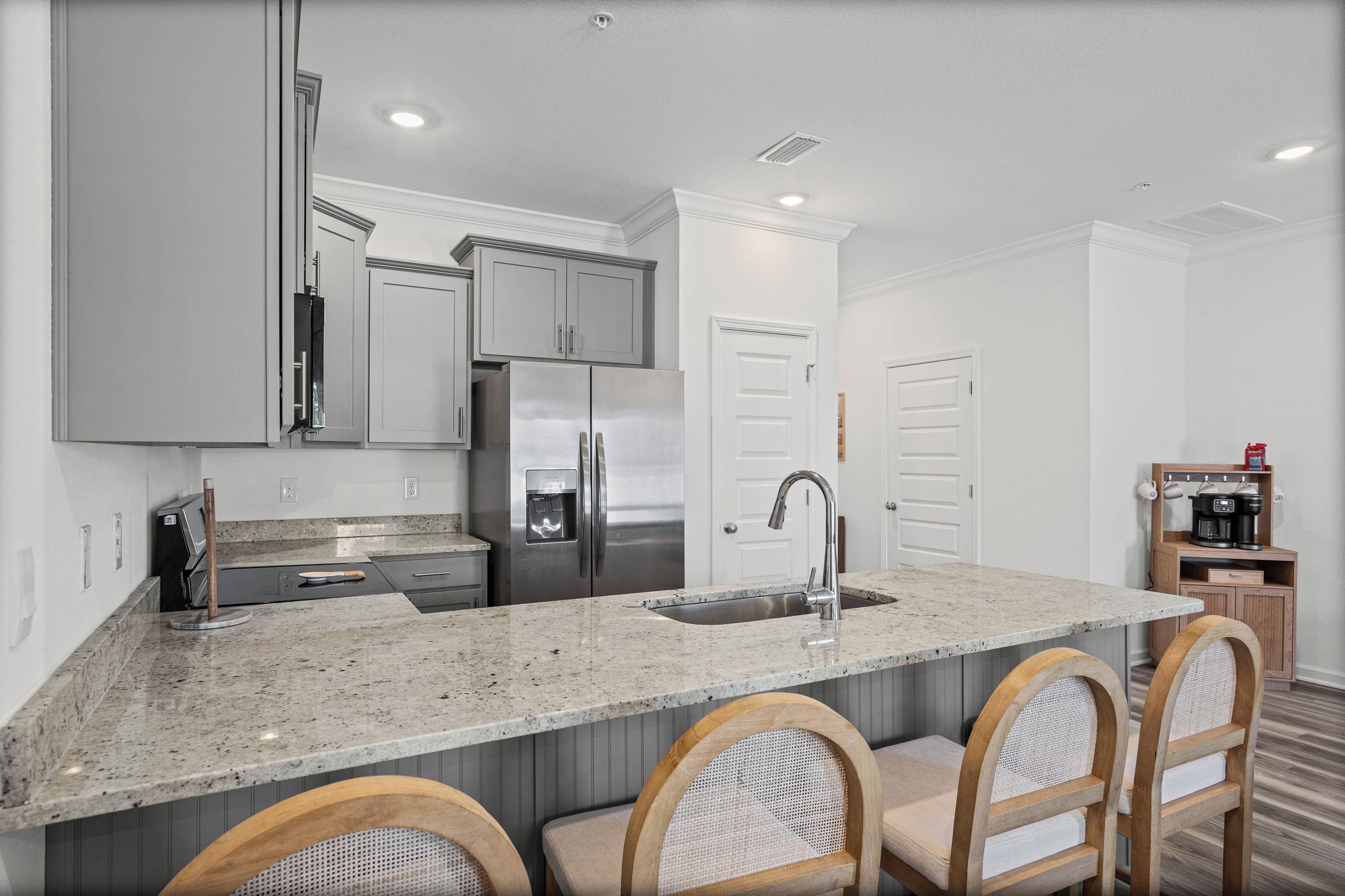 A modern kitchen with a granite countertop, stainless steel appliances, and a bar area with wooden chairs.