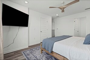 Ein Schlafzimmer mit einem Bett, einem Deckenventilator, einem an der Wand befestigten Fernseher und einem gemusterten Teppich.