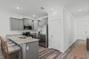 A modern kitchen with a central island, stainless steel appliances, and a grey backsplash. - The Cove-3-bedroom townhome in Orange Beach. Pet friendly! (Orange Beach)