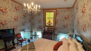 A bedroom with a large bed, a chandelier, a television, a piano, and floral wallpaper. - Escape to The Pella Mansion: Peaceful Countryside Estate, AC, Close to Pella, IA (Pella)