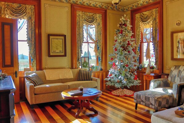 A cozy living room with a wooden floor, a sofa, a chair, and a Christmas tree.