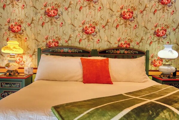 A bed with floral wallpaper, two bedside lamps, and a red pillow.