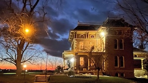 A historic building with a prominent tower, a covered porch, and a well-lit entrance. - Escape to The Pella Mansion: Peaceful Countryside Estate, AC, Close to Pella, IA (Pella)