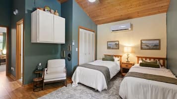 A room with two beds, a chair, a wardrobe, and an air conditioning unit.