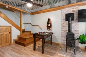 Een kamer met een houten trap, een tafelvoetbaltafel, een stenen muur en een houtkachel.