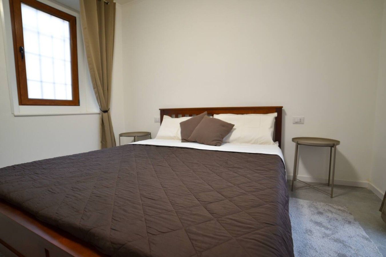 A bedroom with a large bed, a window with curtains, and two bedside tables.