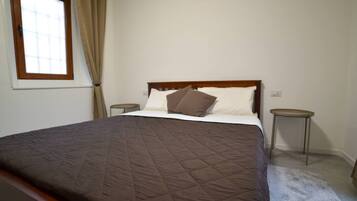 A bedroom with a large bed, a window with curtains, and two bedside tables.