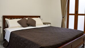 A single bed with a wooden headboard, a dark quilted bedspread, and two pillows. - Fly&Rest MXP | Unit 1 | 24/7 Airport Transfer (Casorate Sempione)