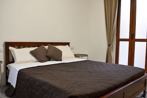 Een enkel bed met een houten hoofdbord, een donkere gewatteerde spreideken en twee kussens.