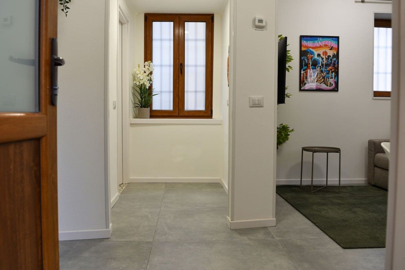 Ein Flur mit einer Holztür, einem Fenster mit Blumentopf, einem kleinen Tisch und einem Gemälde an der Wand.