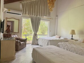 A bedroom with two beds, a sofa, a lamp, and a view of greenery outside.