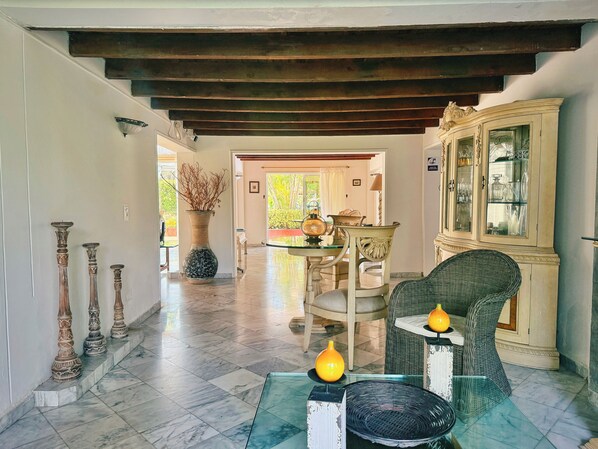A spacious interior with a high ceiling, a dining area with a table and chairs, and a decorative cabinet with glass doors.