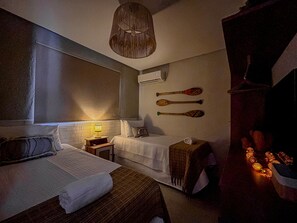 A hotel room with two beds, a bedside table with a lamp, a wall-mounted air conditioner, and a wooden headboard. - Casa Linda quase que pe na Areia (Sao Miguel dos Milagres)