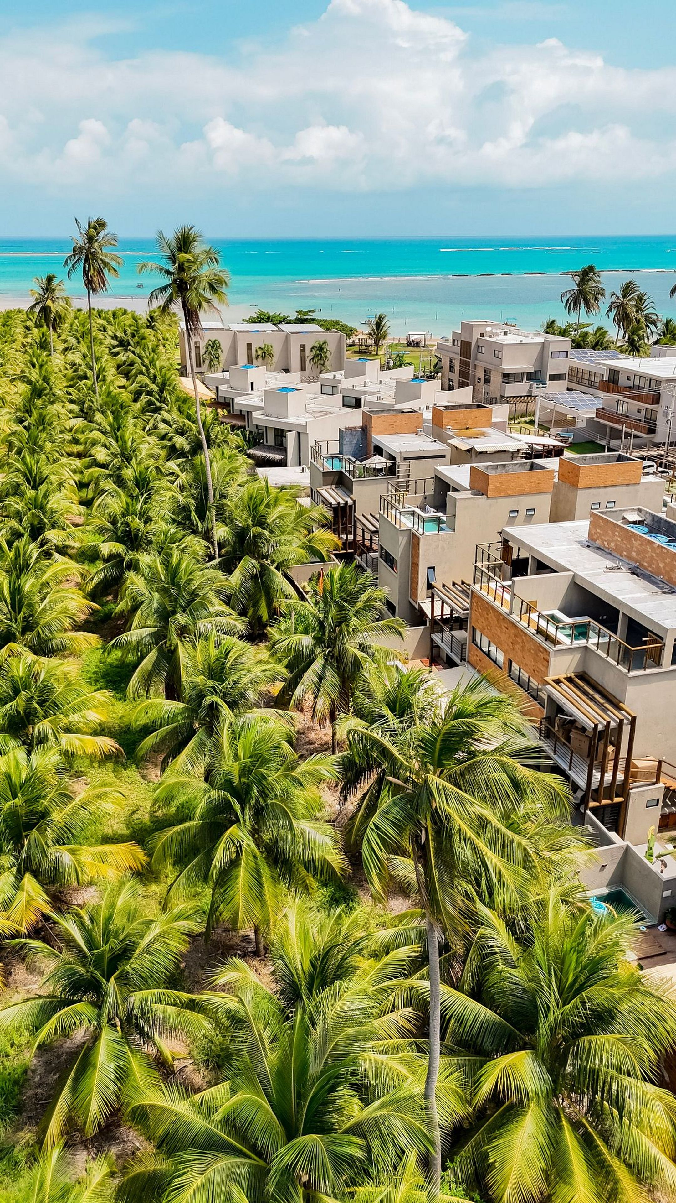 A coastal residential area with modern buildings, a beach, and palm trees.