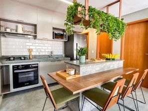 A modern kitchen with a central island, stainless steel appliances, and a wooden dining table with chairs. - Casa Linda quase que pe na Areia (Sao Miguel dos Milagres)